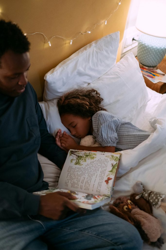 A father reading a bedtime story to his daughter, who is sleeping peacefully in bed.